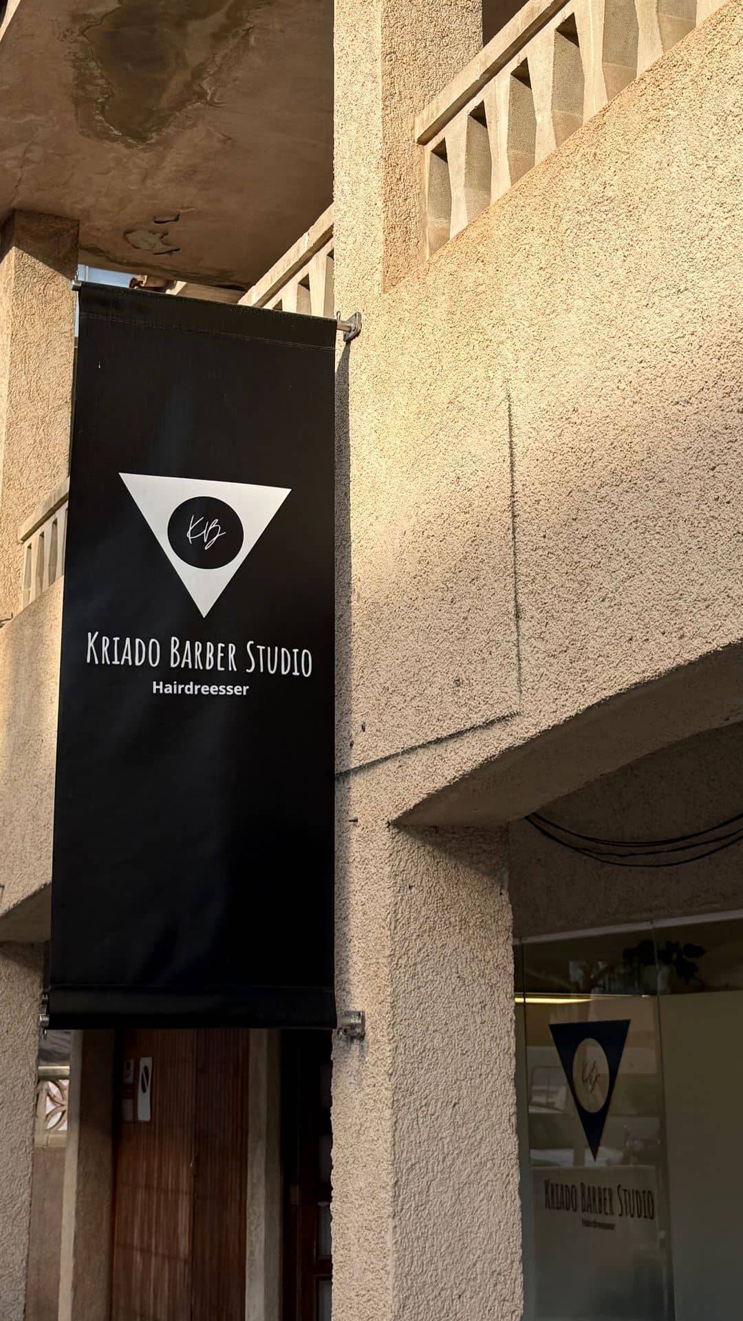Fachada de Kriado Studio en Carrer Leonor Servera 7, Cala Ratjada, con la banderola negra de Kriado Barber Studio